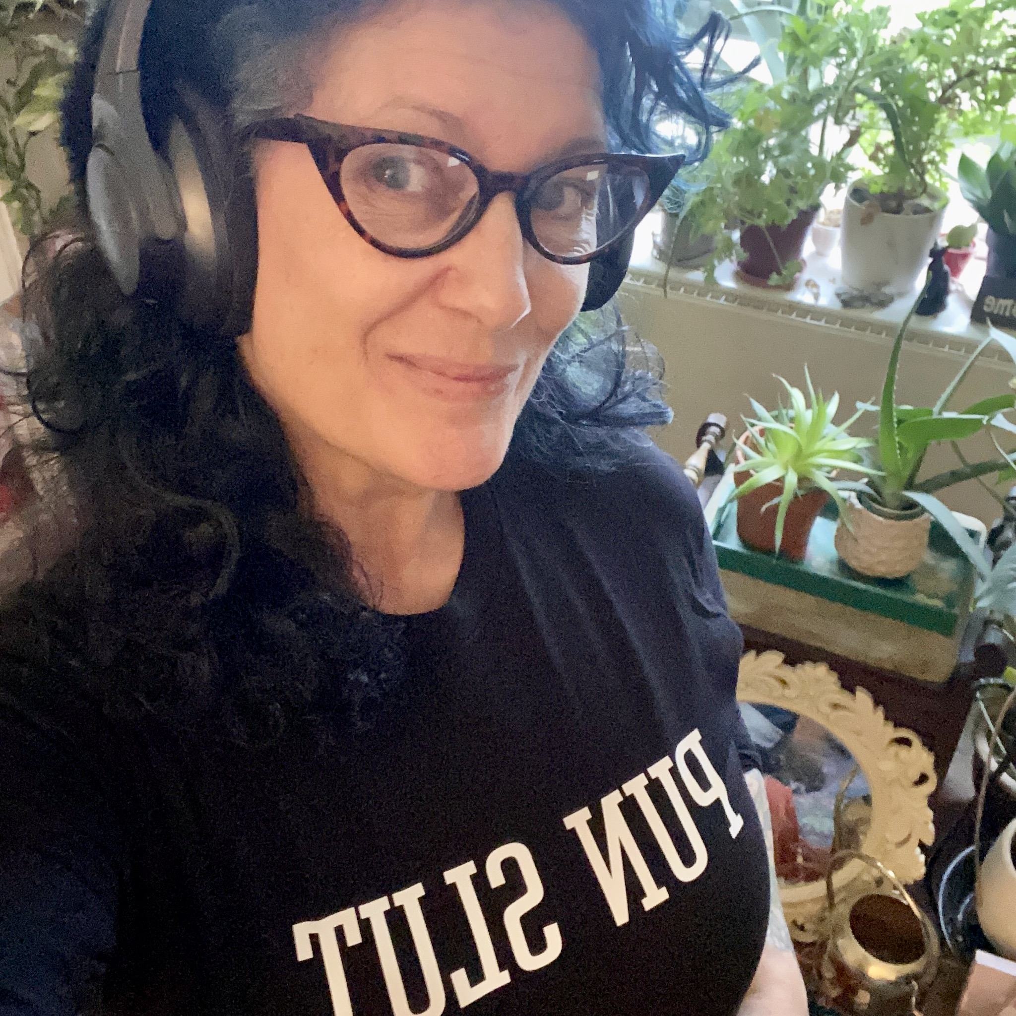 headshot of Jet Moon, a genderqueer femme with dark blue hair wearing glasses and a t-shirt that says PUN SLUT